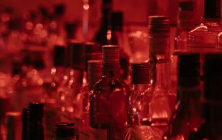 ampolles d’alcohol en un bar amb llum vermella representant el consum social i els efectes estimulants inicials de l’alcohol